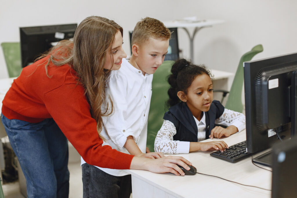 Lehrkraft zeigt Kindern etwas am Computer